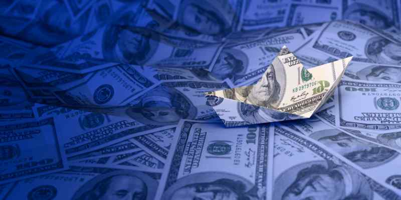A paper boat crafted from a hundred-dollar bill sits on a sea of cash, symbolizing savings and risk.