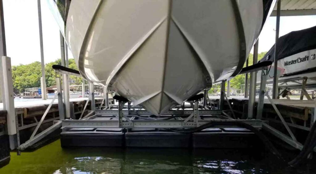 Bow of a white boat resting on bunks above black poly tanks and a galvanized frame on a floating boat lift at Lake of the Ozarks.